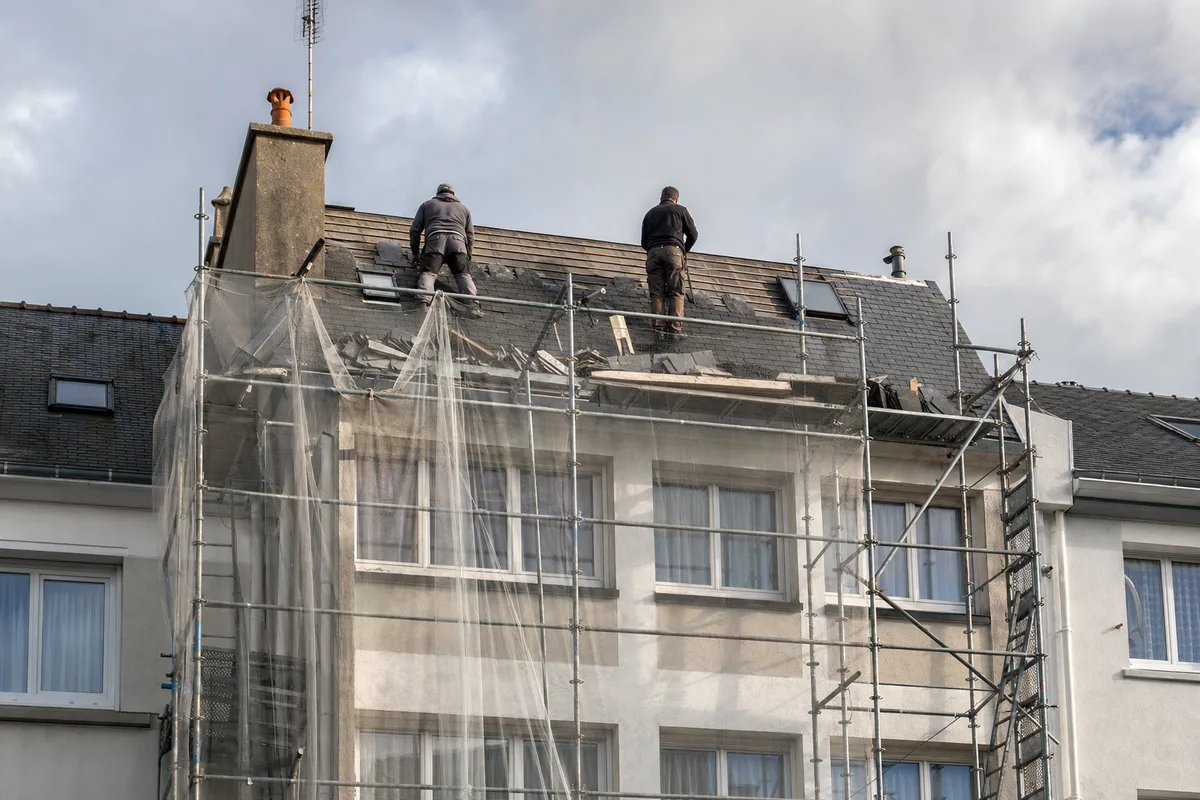 Échafaudage dressé contre un immeuble brestois, couvreurs au travail sur une toiture d’ardoise