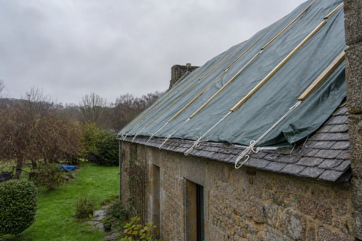 Bâche de protection tendue sur une toiture bretonne en attente de réparation